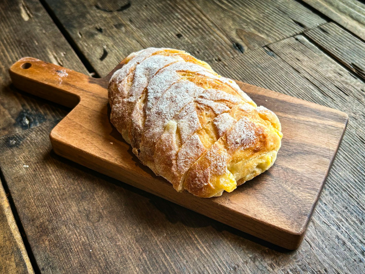 Una pagnotta dorata riposa su un tagliere di legno.