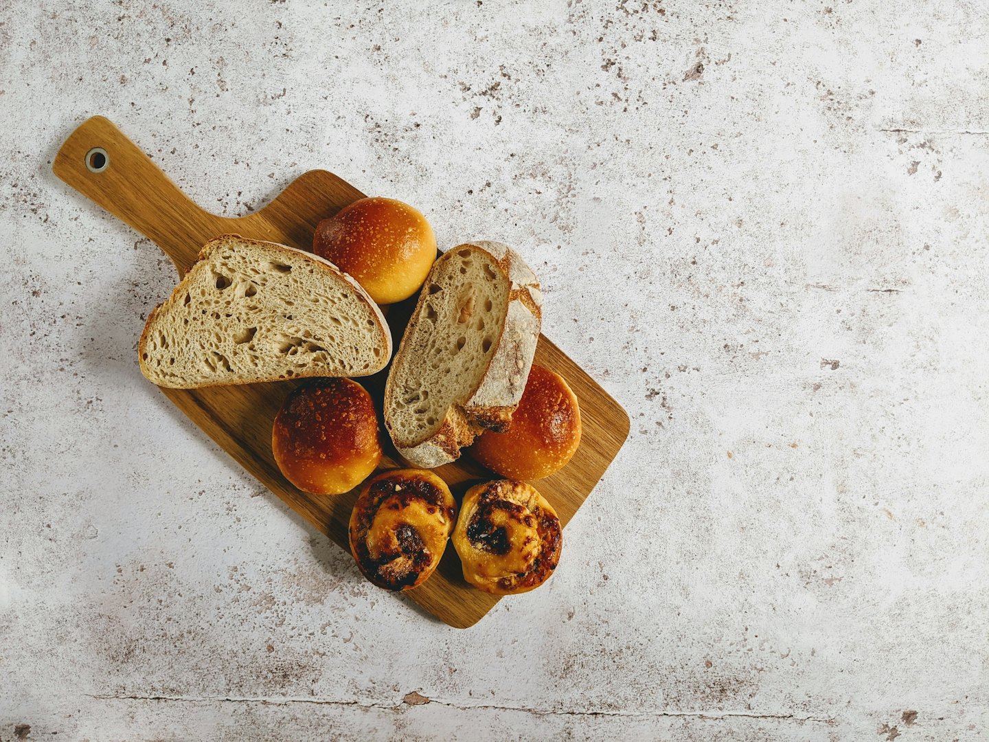 Pane artigianale e pasticcini appena sfornati su un tagliere di legno.
