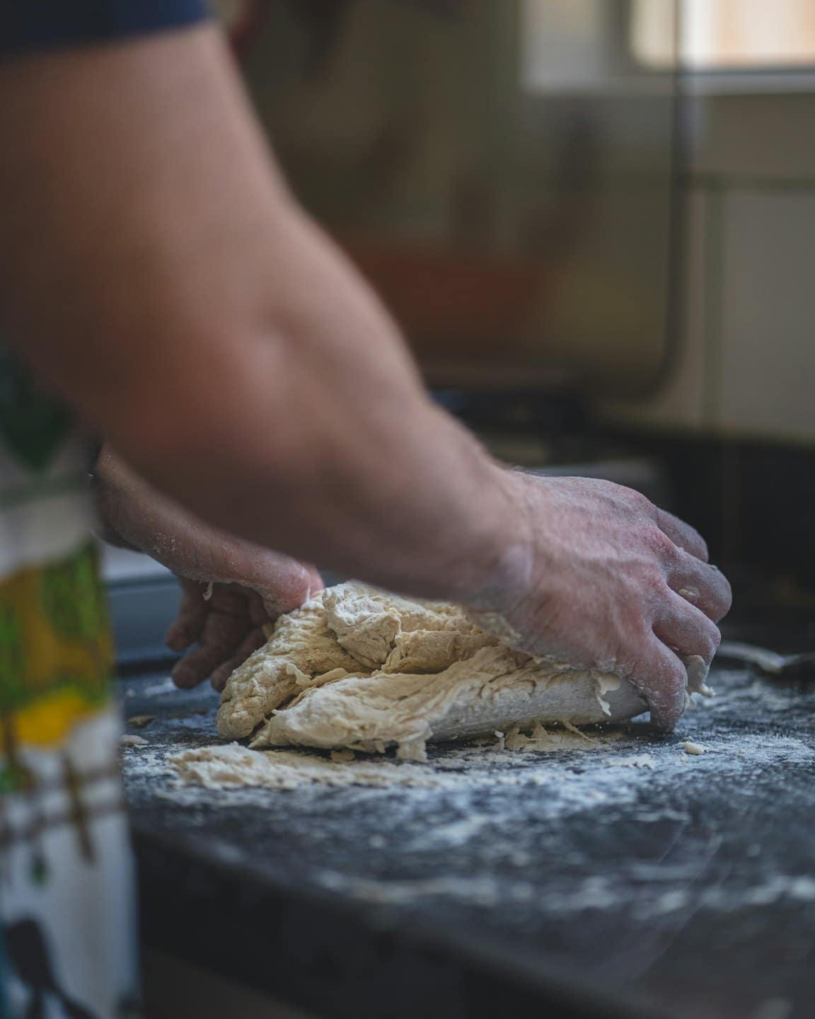 Mani che impastano pasta fresca su un bancone da cucina infarinato.