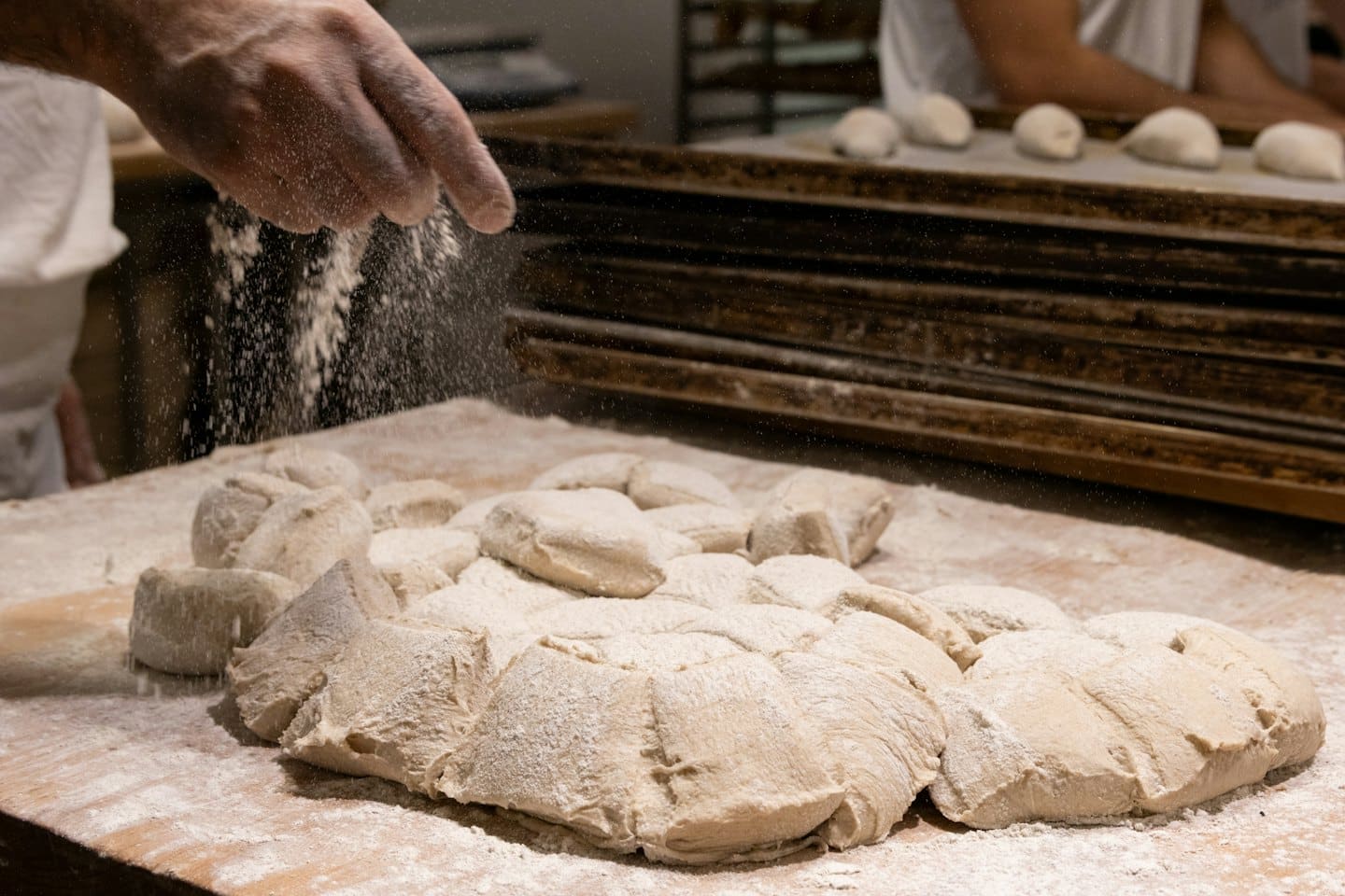 Un fornaio spolvera farina su un impasto su un tavolo di legno.