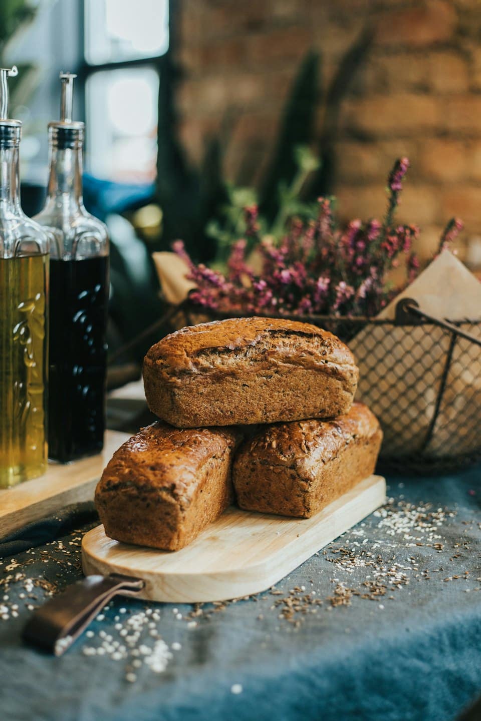 Tre pagnotte rustiche di pane integrale impilate su un tagliere di legno.